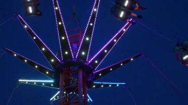 Gece gökyüzüne karşı parlayan ışıklarla süslenmiş canlı bir eğlence gezisi. Luna Parkı. Parlak yeşil ışıklar lunaparktaki dönen bir atlıkarıncanın üzerinde dans ediyor. Ekstrem atlıkarınca neşeyle döner, büyüleyici yeşil ışıklarla aydınlatılır. çekim gücü