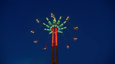 Gece gökyüzüne karşı parlayan ışıklarla süslenmiş canlı bir eğlence gezisi. Luna Parkı. Parlak yeşil ışıklar lunaparktaki dönen bir atlıkarıncanın üzerinde dans ediyor. Ekstrem atlıkarınca neşeyle döner, büyüleyici yeşil ışıklarla aydınlatılır. çekim gücü