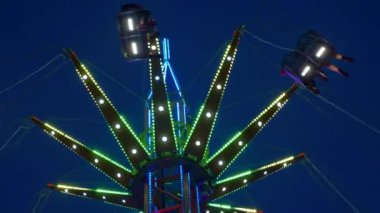 Gece gökyüzüne karşı parlayan ışıklarla süslenmiş canlı bir eğlence gezisi. Luna Parkı. Parlak yeşil ışıklar lunaparktaki dönen bir atlıkarıncanın üzerinde dans ediyor. Ekstrem atlıkarınca neşeyle döner, büyüleyici yeşil ışıklarla aydınlatılır. çekim gücü