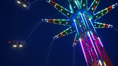 Gece gökyüzüne karşı parlayan ışıklarla süslenmiş canlı bir eğlence gezisi. Luna Parkı. Parlak yeşil ışıklar lunaparktaki dönen bir atlıkarıncanın üzerinde dans ediyor. Ekstrem atlıkarınca neşeyle döner, büyüleyici yeşil ışıklarla aydınlatılır. çekim gücü