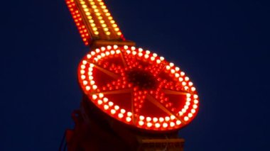 Gece gökyüzüne karşı parlayan ışıklarla süslenmiş canlı bir eğlence gezisi. Luna Parkı. Parlak yeşil ışıklar lunaparktaki dönen bir atlıkarıncanın üzerinde dans ediyor. Ekstrem atlıkarınca neşeyle döner, büyüleyici yeşil ışıklarla aydınlatılır. çekim gücü