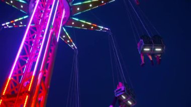 Gece gökyüzüne karşı parlayan ışıklarla süslenmiş canlı bir eğlence gezisi. Luna Parkı. Parlak yeşil ışıklar lunaparktaki dönen bir atlıkarıncanın üzerinde dans ediyor. Ekstrem atlıkarınca neşeyle döner, büyüleyici yeşil ışıklarla aydınlatılır. çekim gücü