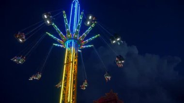 Gece gökyüzüne karşı parlayan ışıklarla süslenmiş canlı bir eğlence gezisi. Luna Parkı. Parlak yeşil ışıklar lunaparktaki dönen bir atlıkarıncanın üzerinde dans ediyor. Ekstrem atlıkarınca neşeyle döner, büyüleyici yeşil ışıklarla aydınlatılır. çekim gücü