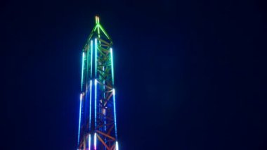 Gece gökyüzüne karşı parlayan ışıklarla süslenmiş canlı bir eğlence gezisi. Luna Parkı. Parlak yeşil ışıklar lunaparktaki dönen bir atlıkarıncanın üzerinde dans ediyor. Ekstrem atlıkarınca neşeyle döner, büyüleyici yeşil ışıklarla aydınlatılır. çekim gücü