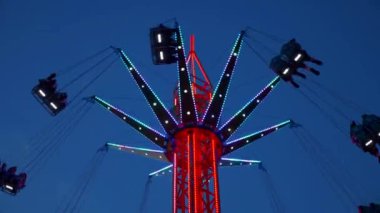 Gece gökyüzüne karşı parlayan ışıklarla süslenmiş canlı bir eğlence gezisi. Luna Parkı. Parlak yeşil ışıklar lunaparktaki dönen bir atlıkarıncanın üzerinde dans ediyor. Ekstrem atlıkarınca neşeyle döner, büyüleyici yeşil ışıklarla aydınlatılır. çekim gücü