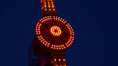 Gece gökyüzüne karşı parlayan ışıklarla süslenmiş canlı bir eğlence gezisi. Luna Parkı. Parlak yeşil ışıklar lunaparktaki dönen bir atlıkarıncanın üzerinde dans ediyor. Ekstrem atlıkarınca neşeyle döner, büyüleyici yeşil ışıklarla aydınlatılır. çekim gücü