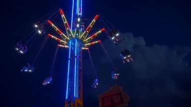 Gece gökyüzüne karşı parlayan ışıklarla süslenmiş canlı bir eğlence gezisi. Luna Parkı. Parlak yeşil ışıklar lunaparktaki dönen bir atlıkarıncanın üzerinde dans ediyor. Ekstrem atlıkarınca neşeyle döner, büyüleyici yeşil ışıklarla aydınlatılır. çekim gücü