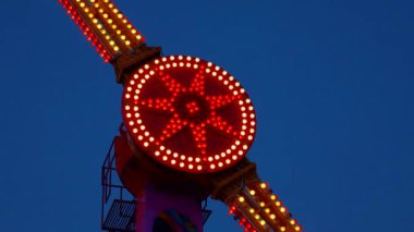 Gece gökyüzüne karşı parlayan ışıklarla süslenmiş canlı bir eğlence gezisi. Luna Parkı. Parlak yeşil ışıklar lunaparktaki dönen bir atlıkarıncanın üzerinde dans ediyor. Ekstrem atlıkarınca neşeyle döner, büyüleyici yeşil ışıklarla aydınlatılır. çekim gücü