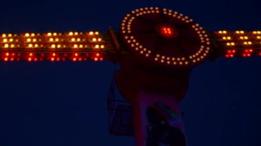 Gece gökyüzüne karşı parlayan ışıklarla süslenmiş canlı bir eğlence gezisi. Luna Parkı. Parlak yeşil ışıklar lunaparktaki dönen bir atlıkarıncanın üzerinde dans ediyor. Ekstrem atlıkarınca neşeyle döner, büyüleyici yeşil ışıklarla aydınlatılır. çekim gücü