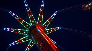Gece gökyüzüne karşı parlayan ışıklarla süslenmiş canlı bir eğlence gezisi. Luna Parkı. Parlak yeşil ışıklar lunaparktaki dönen bir atlıkarıncanın üzerinde dans ediyor. Ekstrem atlıkarınca neşeyle döner, büyüleyici yeşil ışıklarla aydınlatılır. çekim gücü