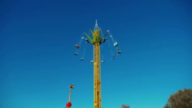 Mavi gökyüzüne karşı parlayan ışıklarla süslenmiş canlı bir eğlence gezisi. Luna Parkı. Lunaparktaki dönme dolap. Ekstrem atlıkarınca sevinçle dönüyor. Güneşli bir gökyüzünde yeşil ışıklarla parıldayan neşeli bir eğlence..