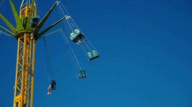 Mavi gökyüzüne karşı parlayan ışıklarla süslenmiş canlı bir eğlence gezisi. Luna Parkı. Lunaparktaki dönme dolap. Ekstrem atlıkarınca sevinçle dönüyor. Güneşli bir gökyüzünde yeşil ışıklarla parıldayan neşeli bir eğlence..