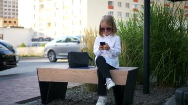 Genç bir kız şık güneş gözlüğü takıyor, akıllı telefonuyla oynuyor ve çok mutlu. Güneş gözlüklü mutlu bir kız telefonunda mesaj atıyor. İş kadını, internette iletişim.