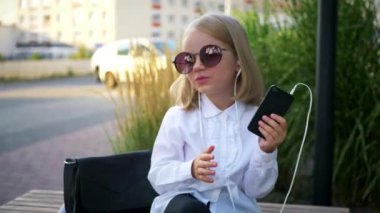 Genç bir kız elinde telefonuyla mutlu, komik bir şekilde dans ediyor ve kulaklıklarıyla müziğin tadını çıkarıyor. Genç bir iş kadını, iş merkezinin yakınında telefonu elinde tutarak mutlu olur. Kulaklık takan şık bir çocuk., 