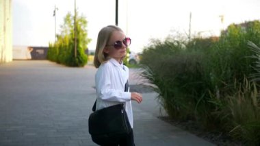 Beyaz gömlekli ve siyah pantolonlu genç bir kız sokaktaki bir iş merkezinin arka planında komik bir şekilde dans ediyor. Genç iş kadını mutlu. Kendi dünyasına dalmış şık bir çocuk