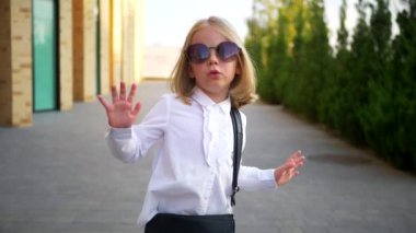 Beyaz gömlekli ve siyah pantolonlu genç bir kız sokaktaki bir iş merkezinin arka planında komik bir şekilde dans ediyor. Genç iş kadını mutlu. Kendi dünyasına dalmış şık bir çocuk