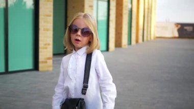 Beyaz gömlekli ve siyah pantolonlu genç bir kız sokaktaki bir iş merkezinin arka planında komik bir şekilde dans ediyor. Genç iş kadını mutlu. Kendi dünyasına dalmış şık bir çocuk