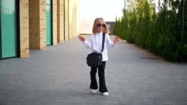 Beyaz gömlekli ve siyah pantolonlu genç bir kız sokaktaki bir iş merkezinin arka planında komik bir şekilde dans ediyor. Genç iş kadını mutlu. Kendi dünyasına dalmış şık bir çocuk