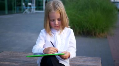 Tabletine odaklanmış, bankta oturan genç bir kız. Bir kız parkta bankta otururken mutlu ve tabletinin tadını çıkarıyor. İş kadını. Tablet cihazıyla meşgul bir çocuk bankta oturuyor..