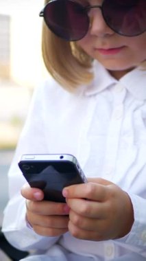 Dikey, şık güneş gözlüğü takan genç bir kız akıllı telefonuyla oynuyor ve çok mutlu. Güneş gözlüklü mutlu bir kız telefonunda mesaj atıyor. İş kadını, internette iletişim.