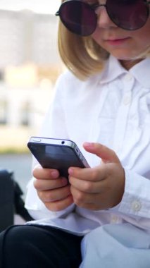 Dikey, şık güneş gözlüğü takan genç bir kız akıllı telefonuyla oynuyor ve çok mutlu. Güneş gözlüklü mutlu bir kız telefonunda mesaj atıyor. İş kadını, internette iletişim.
