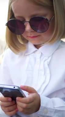 Dikey, şık güneş gözlüğü takan genç bir kız akıllı telefonuyla oynuyor ve çok mutlu. Güneş gözlüklü mutlu bir kız telefonunda mesaj atıyor. İş kadını