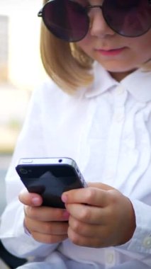 Dikey, şık güneş gözlüğü takan genç bir kız akıllı telefonuyla oynuyor ve çok mutlu. Güneş gözlüklü mutlu bir kız telefonunda mesaj atıyor. İş kadını