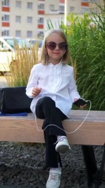 Dikey olarak, genç bir kız elinde telefonuyla mutlu, komik bir şekilde dans ediyor ve kulaklıklarıyla müziğin tadını çıkarıyor. Genç bir iş kadını mutlu, iş yerinin yakınında telefonu elinde tutuyor.