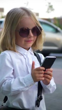 Dikey, şık güneş gözlüğü takan genç bir kız akıllı telefonuyla oynuyor ve çok mutlu. Güneş gözlüklü mutlu bir kız telefonunda mesaj atıyor. İş kadını