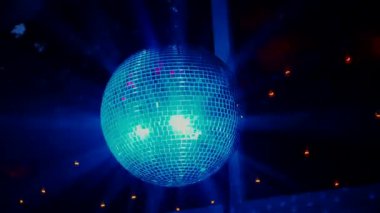 Bir gece kulübünün loş ışıklı odasında asılı duran parıldayan mavi bir disko topu. Mavi bir disko topunun yansıması karanlık bir uzayda dans ediyor. Karanlık bir odanın gölgesinde tek başına parlayan mavi bir disko topu. Derin gölgeler parlak maviyi vurgular.