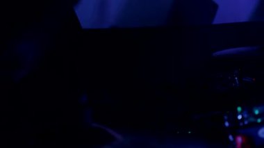 Davulcu cool rock konserini çalar. Bir adam sahnede enerjik bir şekilde davul çalıyor arkasında parlak ışıklar yanıyor. Canlı performans sergileyen bir davulcu. Etrafı renkli sahne ışıklarıyla çevrili. Parlak ışıklarla davul çalan bir adam 
