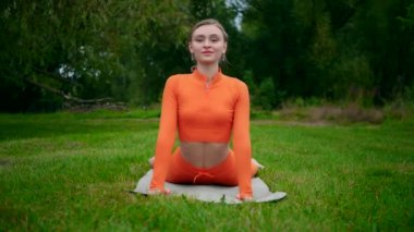 Yoga yaparken parkta gerinen turuncu kıyafetli bir kadın. Esneklik eğitimi, Limbering rutinleri, hareket alıştırmaları, müşterek seferberlik tatbikatları, esneklik egzersizleri, fiziksel egzersizler, spor egzersizleri yapan bir kız.