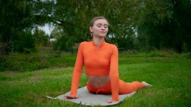 Yoga yaparken parkta gerinen turuncu kıyafetli bir kadın. Esneklik eğitimi, Limbering rutinleri, hareket alıştırmaları, müşterek seferberlik tatbikatları, esneklik egzersizleri, fiziksel egzersizler, spor egzersizleri yapan bir kız.