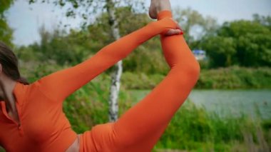 Yoga yaparken parkta gerinen turuncu kıyafetli bir kadın. Esneklik eğitimi, Limbering rutinleri, hareket alıştırmaları, müşterek seferberlik tatbikatları, esneklik egzersizleri, fiziksel egzersizler, spor egzersizleri yapan bir kız.