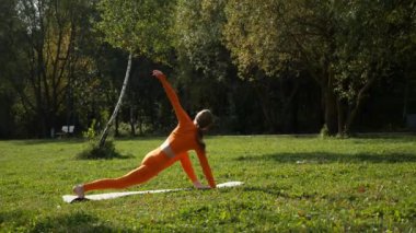 Esneklik eğitimi, Limbering rutinleri, hareket çeşitliliği tatbikatları, müşterek seferberlik tatbikatları, esneklik egzersizleri. Yoga yaparken parkta gerinen turuncu kıyafetli bir kadın. Bir kadın esneme egzersizleri yapar.