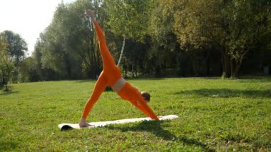 Esneklik eğitimi, Limbering rutinleri, hareket çeşitliliği tatbikatları, müşterek seferberlik tatbikatları, esneklik egzersizleri. Yoga yaparken parkta gerinen turuncu kıyafetli bir kadın. Bir kadın esneme egzersizleri yapar.