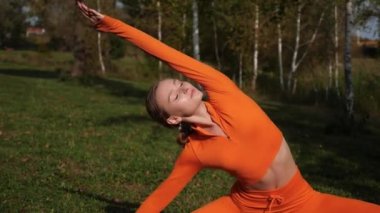 Esneklik eğitimi, Limbering rutinleri, hareket çeşitliliği tatbikatları, müşterek seferberlik tatbikatları, esneklik egzersizleri. Yoga yaparken parkta gerinen turuncu kıyafetli bir kadın. Bir kadın esneme egzersizleri yapar.