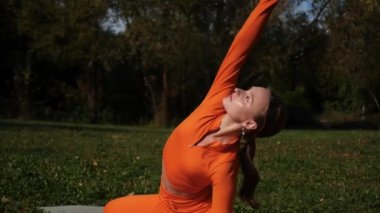 Esneklik eğitimi, Limbering rutinleri, hareket çeşitliliği tatbikatları, müşterek seferberlik tatbikatları, esneklik egzersizleri. Yoga yaparken parkta gerinen turuncu kıyafetli bir kadın. Bir kadın esneme egzersizleri yapar.