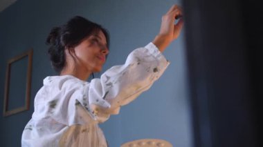 Gülümseyen bir sanatçı sehpaya resim çizer. Mutlu bir kadın tuvalde bir resim yaratıyor. Kadın, sanat stüdyosundaki beyaz kağıda gülüyor ve soyutlama çiziyor..