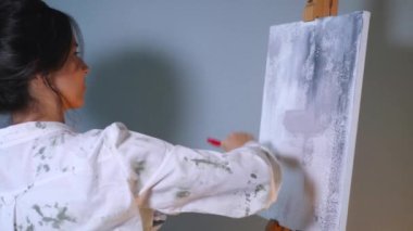 Sanatçı, sehpada beyaz bir tuval üzerinde bir fırça ile soyut bir tablo çizer. Beyaz bluzlu bir kadın stüdyoda parlak renklerle bir resim çiziyor. Sanatçının eli zarafetle hareket eder, tuvale bir güzellik sahnesi çizer. 