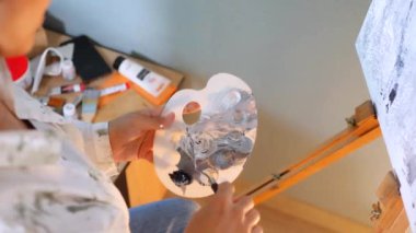 Makro fırça ve palet ve boya. Sanatçı tuvalde bir resim yaratıyor. Bir kadın, bir sanat stüdyosundaki beyaz kağıda soyut bir resim çiziyor..