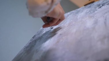 Sanatçı, sehpada beyaz bir tuval üzerinde bir fırça ile soyut bir tablo çizer. Beyaz bluzlu bir kadın stüdyoda parlak renklerle bir resim çiziyor. Sanatçının eli zarafetle hareket eder, tuvale bir güzellik sahnesi çizer. 