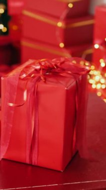 Masadaki Noel ağacının önündeki dikey, kırmızı hediye kutusu. Ağaç zeminli kırmızı hediye kutusu. Masanın üstünde Noel ağacı ve kırmızı hediye var. Şenlik ağacının yanında canlı kırmızı hediye kutusu.