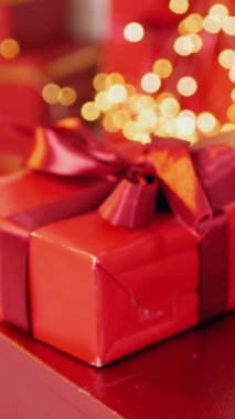 Masadaki Noel ağacının önündeki dikey, kırmızı hediye kutusu. Ağaç zeminli kırmızı hediye kutusu. Masanın üstünde Noel ağacı ve kırmızı hediye var. Şenlik ağacının yanında canlı kırmızı hediye kutusu.