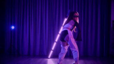 Baştan çıkarıcı dans eden seksi kadın. Titreyen bir dansçı, canlı mor ve mavi ışıkla yıkanmış, canlı neon bir üçgenin altında sahnenin enerjisini somutlaştırıyor. Bir sanatçının kadın vücudu, twerk ve yüksek topuklu ayakkabı sanatının bir kanıtı.