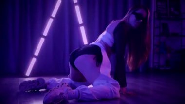 Baştan çıkarıcı dans eden seksi kadın. Titreyen bir dansçı, canlı mor ve mavi ışıkla yıkanmış, canlı neon bir üçgenin altında sahnenin enerjisini somutlaştırıyor. Bir sanatçının kadın vücudu, twerk ve yüksek topuklu ayakkabı sanatının bir kanıtı.