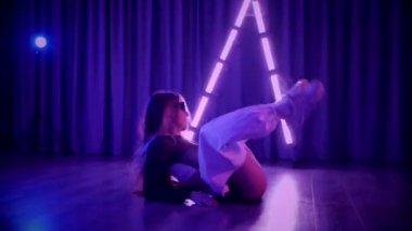 Baştan çıkarıcı dans eden seksi kadın. Titreyen bir dansçı, canlı mor ve mavi ışıkla yıkanmış, canlı neon bir üçgenin altında sahnenin enerjisini somutlaştırıyor. Bir sanatçının kadın vücudu, twerk ve yüksek topuklu ayakkabı sanatının bir kanıtı.