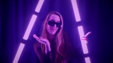 Baştan çıkarıcı dans eden seksi kadın. Titreyen bir dansçı, canlı mor ve mavi ışıkla yıkanmış, canlı neon bir üçgenin altında sahnenin enerjisini somutlaştırıyor. Bir sanatçının kadın vücudu, twerk ve yüksek topuklu ayakkabı sanatının bir kanıtı.