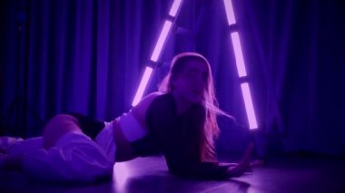 Baştan çıkarıcı dans eden seksi kadın. Titreyen bir dansçı, canlı mor ve mavi ışıkla yıkanmış, canlı neon bir üçgenin altında sahnenin enerjisini somutlaştırıyor. Bir sanatçının kadın vücudu, twerk ve yüksek topuklu ayakkabı sanatının bir kanıtı.