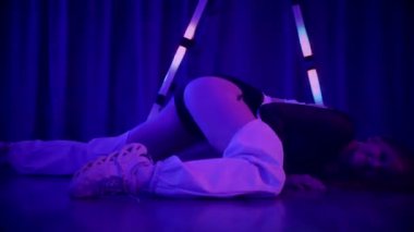 Baştan çıkarıcı dans eden seksi kadın. Titreyen bir dansçı, canlı mor ve mavi ışıkla yıkanmış, canlı neon bir üçgenin altında sahnenin enerjisini somutlaştırıyor. Bir sanatçının kadın vücudu, twerk ve yüksek topuklu ayakkabı sanatının bir kanıtı.